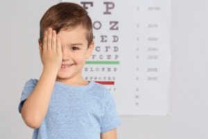 small child with hand over eye standing in front of eye chart